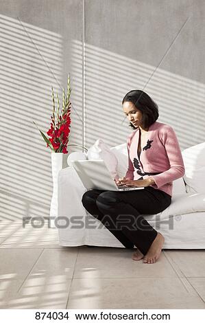 A woman sitting on a sofa using a laptop View Large Photo Image Picture - A woman sitting on a sofa using a laptop. Fotosearch