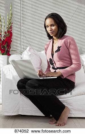 A woman sitting on a sofa using a laptop View Large Photo Image Stock Image - A woman sitting on a sofa using a laptop. Fotosearch