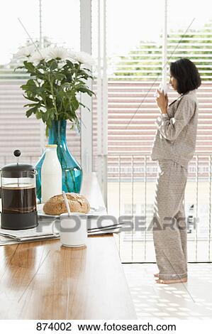 Breakfast on a kitchen counter and a women in pajamas drinking coffee View Large Photo Image Stock Image - Breakfast on a kitchen counter and a women in pajamas drinking coffee. Fotosearch