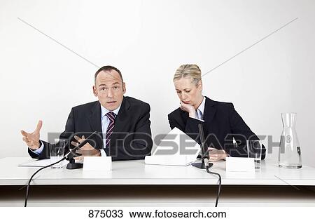 A man and a woman sitting at a desk with microphones and documents View Large Photo Image Stock Image - A man and a woman sitting at a desk with microphones and documents. Fotosearch