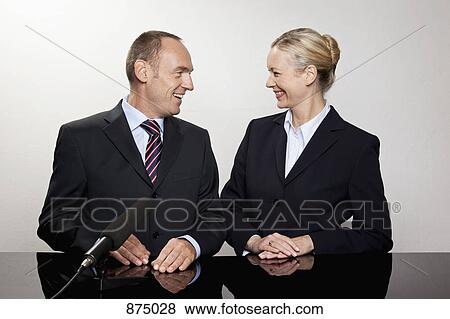 A man and a woman sitting at a desk with a microphone View Large Photo Image Stock Photo - A man and a woman sitting at a desk with a microphone. Fotosearch