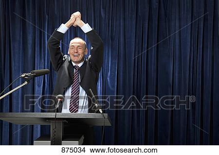 A man in a suit cheering at a lectern View Large Photo Image Picture - A man in a suit cheering at a lectern. Fotosearch