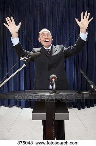 Stock Image - A man in a suit gesturing at a lectern. Fotosearch