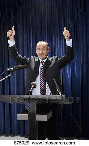 Stock Photo - A man in a suit gesturing at a lectern. Fotosearch