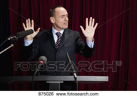 A man in a suit gesturing at a lectern View Large Photo Image Stock Photograph - A man in a suit gesturing at a lectern. Fotosearch