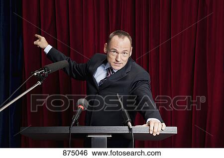 A man in a suit gesturing at a lectern View Large Photo Image Stock Photograph - A man in a suit gesturing at a lectern. Fotosearch