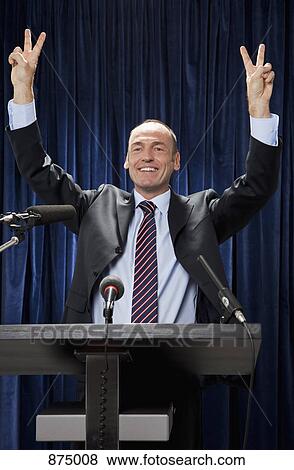 Stock Photo - A man in a suit standing at a lectern and gesturing. Fotosearch