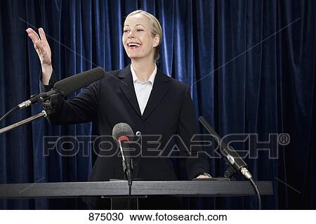 A woman in a suit gesturing at a lectern View Large Photo Image Stock Image - A woman in a suit gesturing at a lectern. Fotosearch