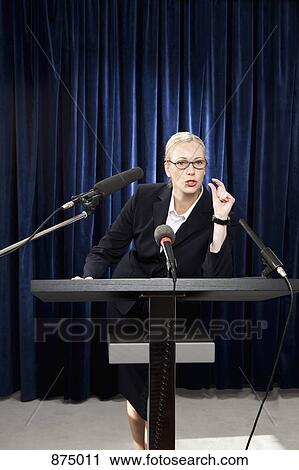 A woman in a suit speaking at a lectern View Large Photo Image Stock Image - A woman in a suit speaking at a lectern. Fotosearch