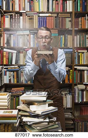 Stock Photo - A man blowing dust off an old book. Fotosearch
