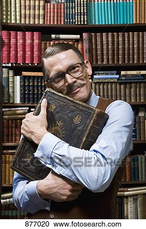 A man holding a book tightly to his chest happily in a bookstore View Large Photo Image Stock Image - A man holding a book tightly to his chest happily in a bookstore. Fotosearch