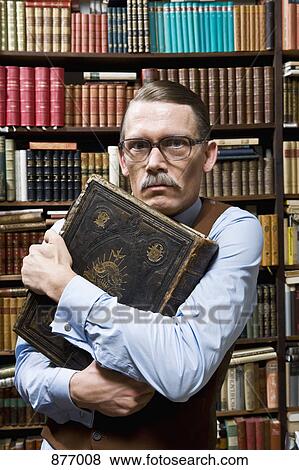 A man holding a book tightly to his chest and looking suspicious in a bookstore View Large Photo Image Stock Photo - A man holding a book tightly to his chest and looking suspicious in a bookstore. Fotosearch