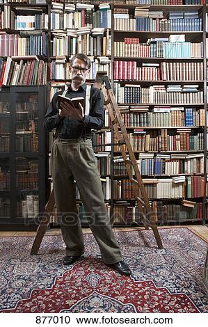 A man standing in a bookstore reading a book View Large Photo Image Stock Image - A man standing in a bookstore reading a book. Fotosearch