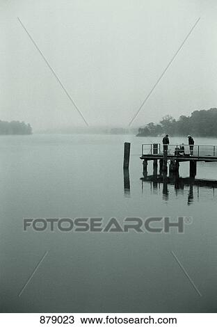 Two men on a pier fishing in a lake View Large Photo Image Stock Image - Two men on a pier fishing in a lake. Fotosearch