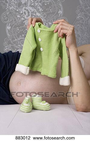 A pregnant woman holding up a baby sweater, midsection View Large Photo Image Stock Image - A pregnant woman holding up a baby sweater, midsection. Fotosearch