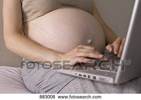 Stock Photo - A pregnant woman using a laptop, midsection, focus on hands. Fotosearch