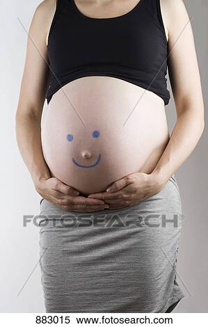 Stock Photography - A smiley face drawn on a pregnant belly, midsection, focus on abdomen. Fotosearch