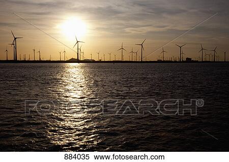 View of wind turbines over water at sunset View Large Photo Image Stock Photography - View of wind turbines over water at sunset. Fotosearch