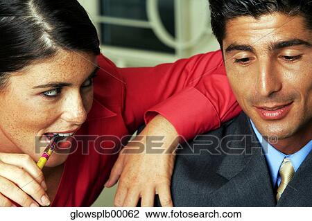 Stock Image - Businessman and businesswoman with arm on man's shoulder and biting pen, close-up. Fotosearch