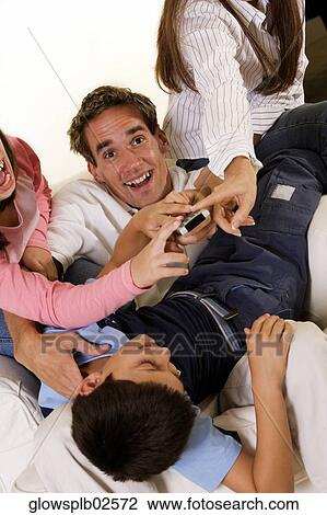Stock Image - Man, boy and two women all trying to use the remote control at the same time. Fotosearch