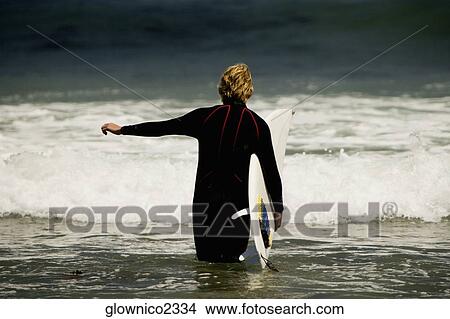 Rear view of a man walking into the sea with a surfboard View Large Photo Image Picture - Rear view of a man walking into the sea with a surfboard. Fotosearch