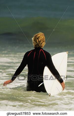 Rear view of a man walking into the sea with a surfboard View Large Photo Image Stock Image - Rear view of a man walking into the sea with a surfboard. Fotosearch