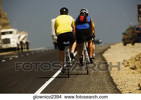 Rear view of two people riding cycles on a road View Large Photo Image Picture - Rear view of two people riding cycles on a road. Fotosearch
