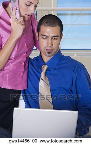 Close-up of a businesswoman talking on a mobile phone with a businessman sitting in front of a laptop View Large Photo Image Stock Image - Close-up of a businesswoman talking on a mobile phone with a businessman sitting in front of a laptop. Fotosearch