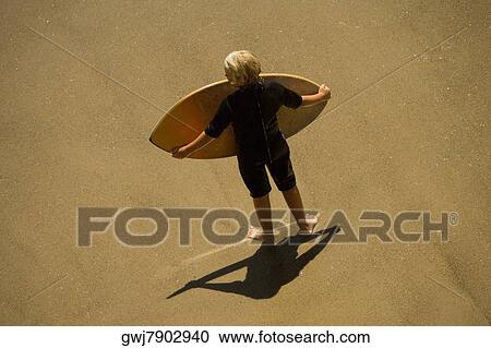 Stock Image - High angle view of a man carrying a boogie board on the beach. Fotosearch
