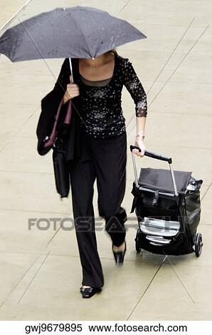 High angle view of a woman walking with an umbrella and suitcase View Large Photo Image Stock Photography - High angle view of a woman walking with an umbrella and suitcase. Fotosearch