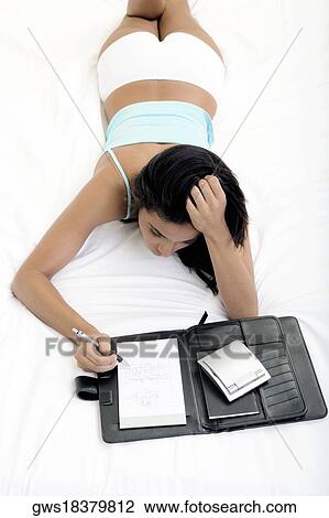 High angle view of a young woman lying on a bed and writing in a personal organizer View Large Photo Image Stock Image - High angle view of a young woman lying on a bed and writing in a personal organizer. Fotosearch