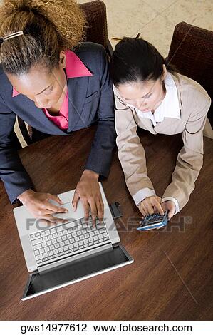 Stock Image - High angle view of two businesswomen using a laptop and a calculator. Fotosearch