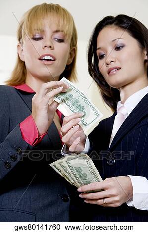 Stock Image - Low angle view of a businesswoman giving a dollar bill to another businesswoman. Fotosearch