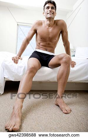 Low angle view of a mid adult man sitting on a bed View Large Photo Image Stock Photo - Low angle view of a mid adult man sitting on a bed. Fotosearch