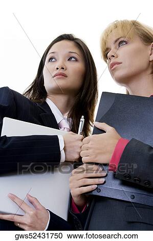 Low angle view of two businesswomen holding a laptop and a file View Large Photo Image Stock Image - Low angle view of two businesswomen holding a laptop and a file. Fotosearch