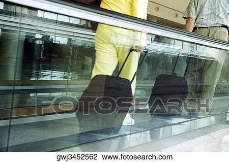 Stock Image - Low section view of two people with luggage on an escalator. Fotosearch