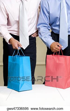 Stock Photography - Mid section view of two businessmen holding shopping bags. Fotosearch