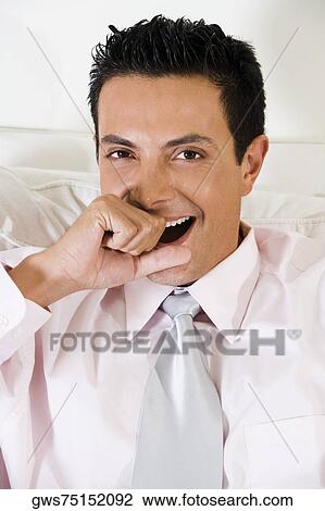 Stock Image - Portrait of a businessman covering his mouth with his hand while yawning. Fotosearch