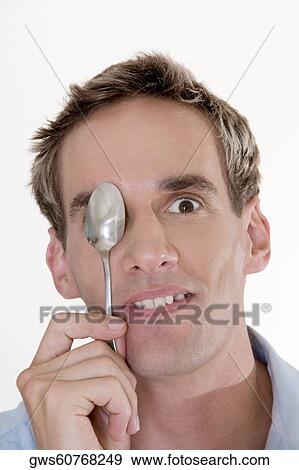 Stock Photo - Portrait of a mid adult man holding a spoon in front of his eye. Fotosearch