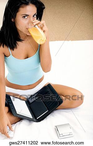 Portrait of a young woman sitting on a bed drinking orange juice View Large Photo Image Stock Image - Portrait of a young woman sitting on a bed drinking orange juice. Fotosearch