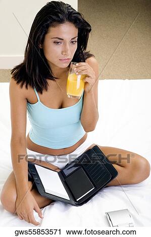 Portrait of a young woman sitting on a bed holding a glass of orange juice View Large Photo Image Stock Image - Portrait of a young woman sitting on a bed holding a glass of orange juice. Fotosearch