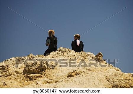 Rear view of two women sitting on a rock by the sea View Large Photo Image Stock Photo - Rear view of two women sitting on a rock by the sea. Fotosearch