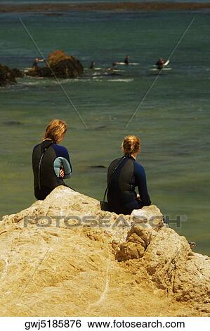 Rear view of two women sitting on a rock by the sea View Large Photo Image Stock Photograph - Rear view of two women sitting on a rock by the sea. Fotosearch