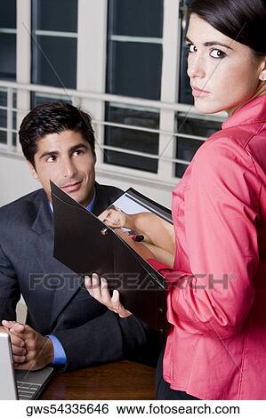 Stock Photograph - Side profile of a businesswoman holding a file with a businessman looking at her. Fotosearch