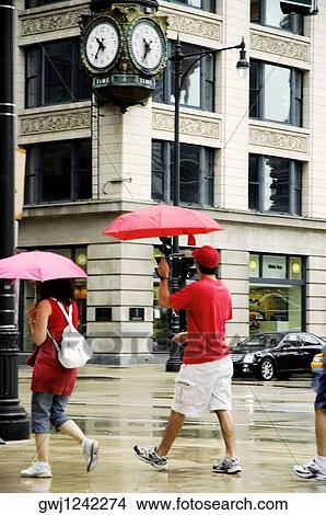Picture - Side profile of pedestrians walking with umbrellas on a sidewalk, Chicago, Illinois, USA. Fotosearch