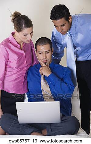 Two businessmen and a businesswoman in front of a laptop View Large Photo Image Stock Photo - Two businessmen and a businesswoman in front of a laptop. Fotosearch