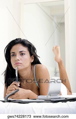 Stock Image - Young woman lying on a bed in front of a personal organizer. Fotosearch
