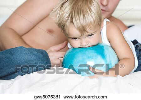 Stock Image - Boy holding a ball and lying on the bed with his father. Fotosearch