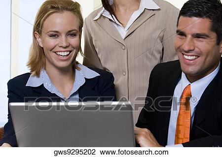 Businessman and two businesswomen in front of a laptop View Large Photo Image Stock Image - Businessman and two businesswomen in front of a laptop. Fotosearch