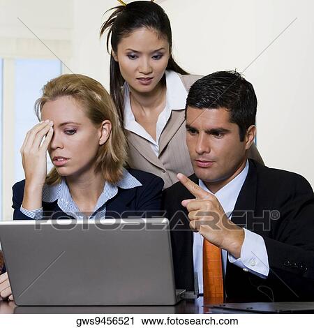 Stock Image - Businessman and two businesswomen looking at a laptop. Fotosearch